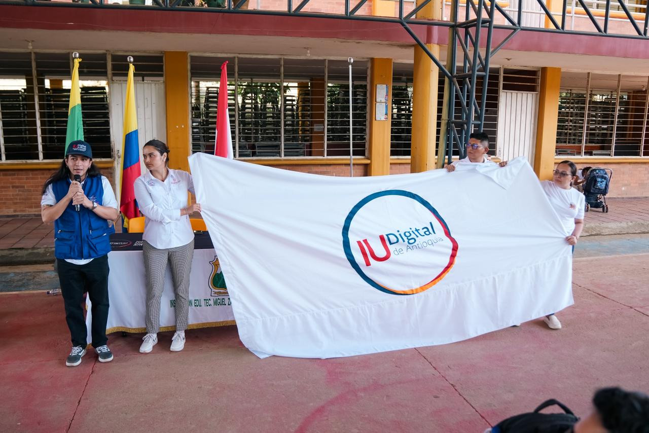 Grupo de estudiantes y equipo de la IU Digital posando frente al mural comunitario en El Plateado, como parte de la estrategia de acompañamiento territorial.