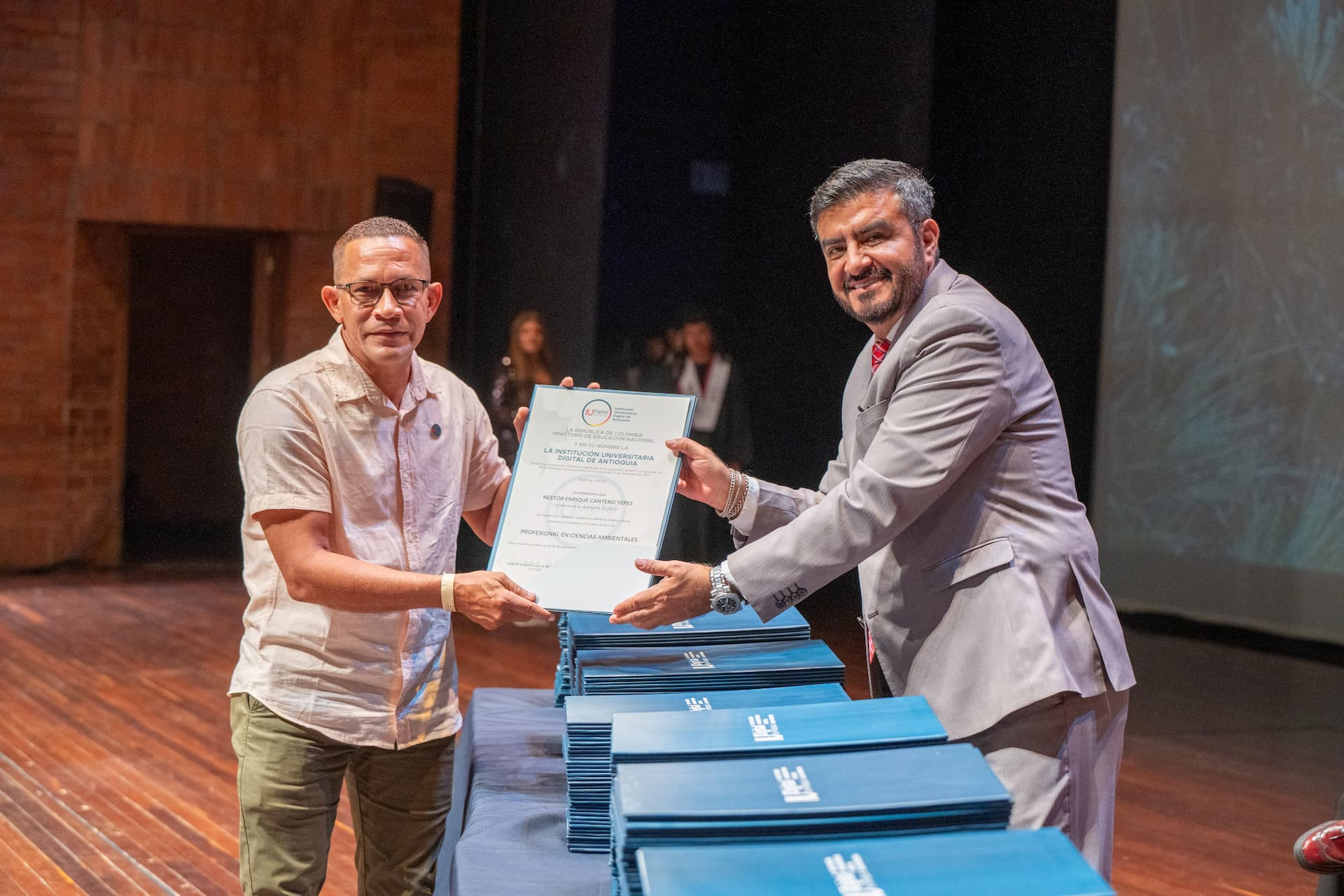Graduado de la IU Digital de Antioquia posa con su diploma junto al Rector de la IU Digital